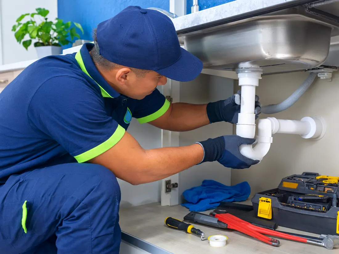 Técnico reparando el sifón bajo un lavaplatos